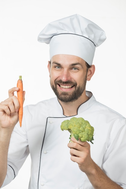 Professional smiling male chef holding fresh organic carrot and green broccoli