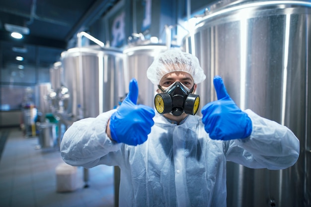 Free photo professional technologist expert in protective white uniform with hairnet, mask and gloves holding both thumbs up