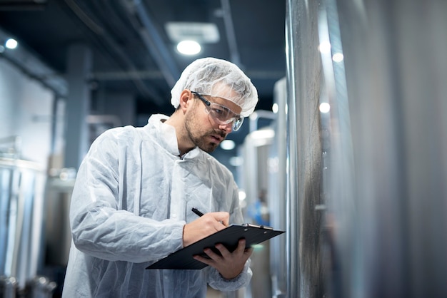 Professional technologist in white protective uniform controlling industrial process at production plant