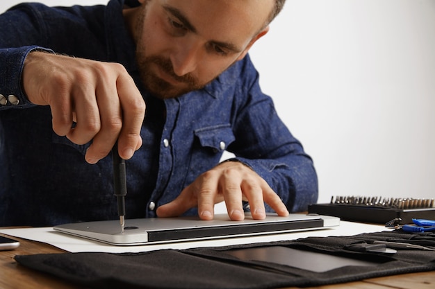 Professional unscrewing case of metallic slim laptop in his electric service lab to clean and repair it