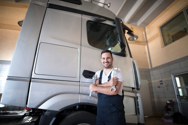 Professional vehicle mechanic standing in workshop with crossed arms and wrench tool ready to start repairing truck