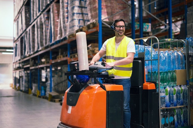 Professional warehouse worker with headset communication equipment driving forklift and relocating packages in storage center