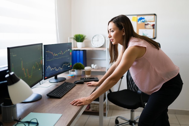 オンラインで株を買う絶好の瞬間を待っているプロの女性。彼女の貿易ビジネスでフリーランサーとして働いているラテン女性の側面図