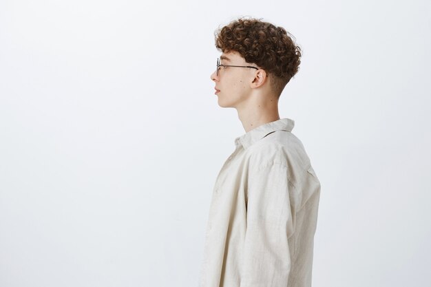 Profile of attractive and stylish teenage guy posing against the white wall