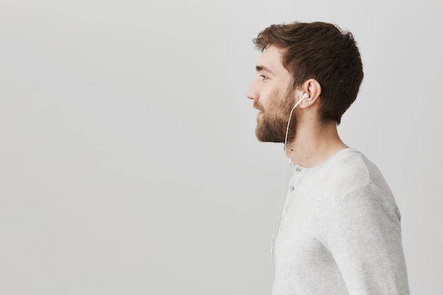 Profile of bearded handsome guy listening music in earphones