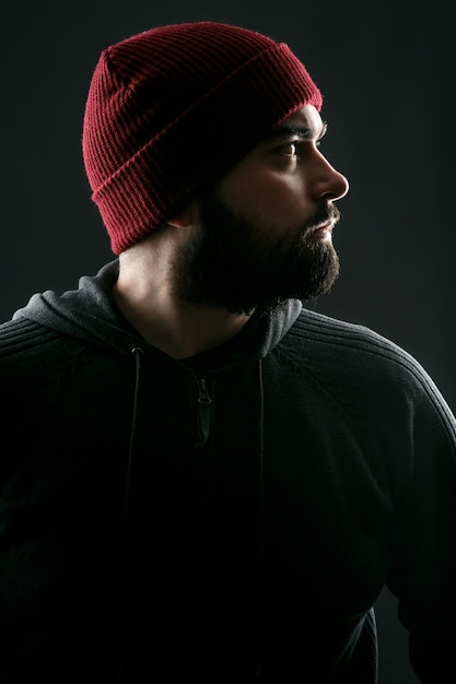 Profile of bearded young man in red hat standing on grey background