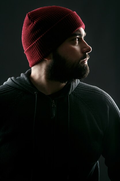 Profile of bearded young man in red hat standing on grey background 