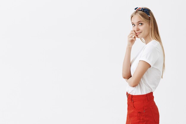 Profile of beautiful young blond girl posing against the white wall