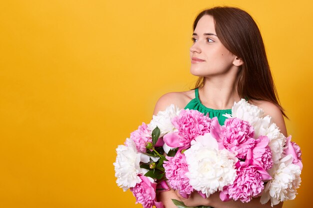 緑の服を着て、牡丹の巨大な花束を抱きしめるブルネットの若い女性のプロフィール