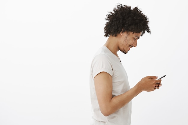 Profile of handsome dark-skinned man texting message with pleased smile, chat in dating app