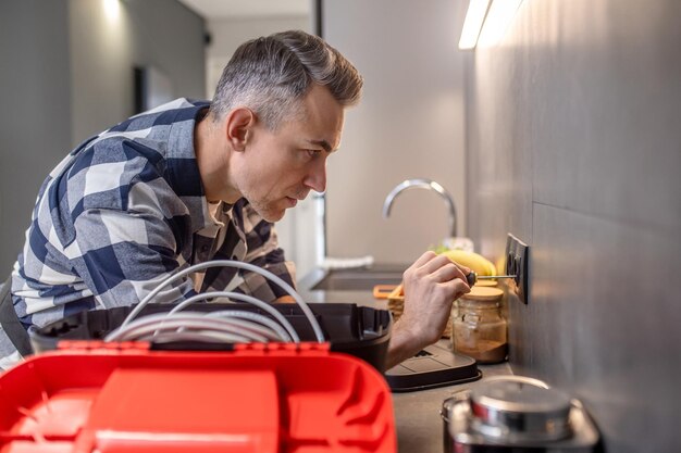 Profile of man touching socket on wall with screwdriver