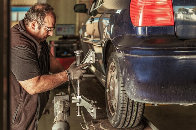 Profile of a mechanic standing while repairing the steering alignment of a blue car in a garage