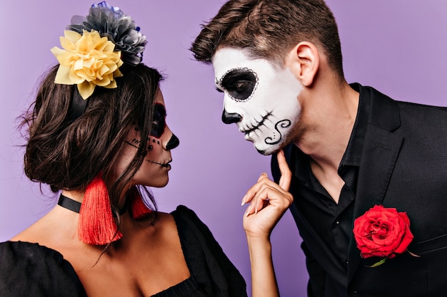 Profile portrait of girl with bright colorful accessories and her man in black jacket with rose in his pocket, looking at each other.