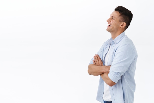 Profile portrait of handsome happy adult family guy in shirt cross hands over chest laughing and smiling pleased looking left empty space at something adorable and funny white background