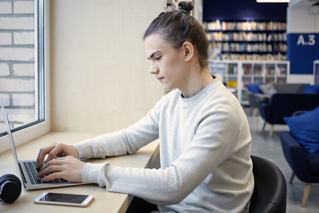 Profile portrait of hardworking concentrated male student with hair knot working on course paper