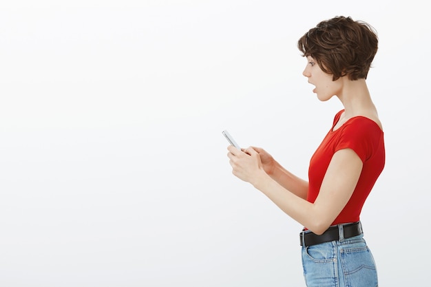 Profile portrait of impressed and shocked woman drop jaw while stare at smartphone screen