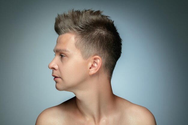 Profile portrait of shirtless young man isolated on grey wall