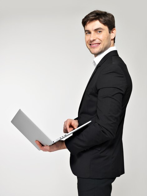Profile portrait of smiling happy businessman with laptop in black suit.