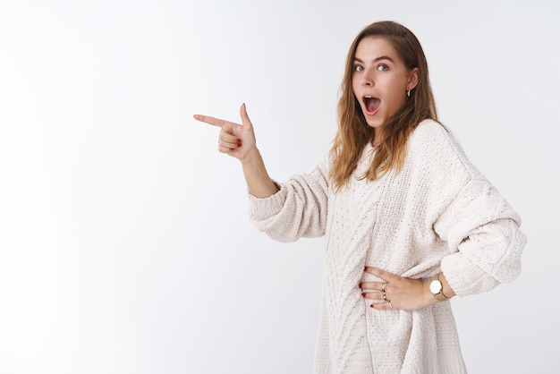 Profile shot amused overwhelmed   woman customer drop jaw impressed pointing sideways direction turning camera astonished standing excited white background.