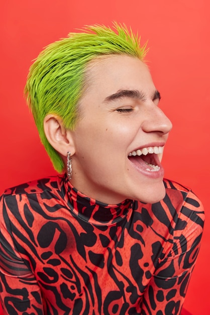 Снимок профиля беззаботной хипстерской девушки, радостно смеющейся, веселится, модная зеленая прическа очень счастлива, экзотическая внешность изолирована над красной стеной