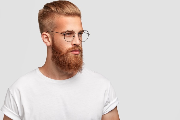 Бесплатное фото Брутальный мужчина с густой лисьей бородой, в круглых очках и задумчиво смотрит в сторону, в профиль.