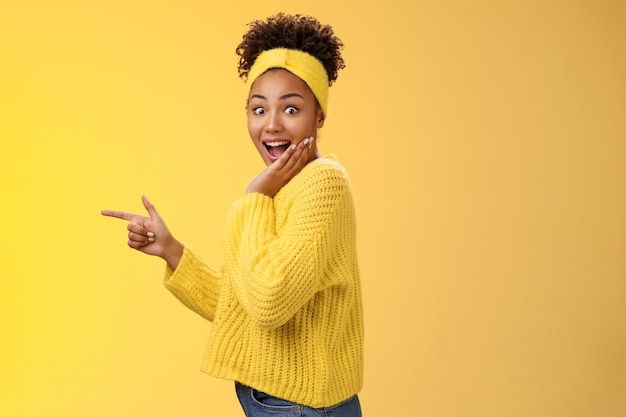 Profile studio shot amused impressed speechless cute stylish shopping girl drop jaw amazed widen eyes turning camera surprised cover open mouth palm pointing left index finger show cool promo.