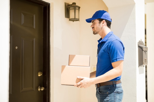 Profile view of an attractive young delivery guy with some packages waiting for the door to open