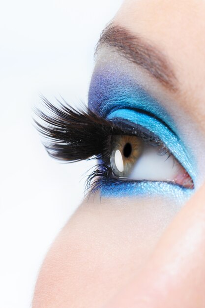 Женский глаз в профиль с ярко-синим макияжем и длинными черными накладными ресницами