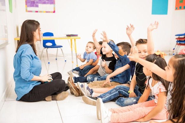 Foto gratuita vista di profilo di un gruppo di studenti in età prescolare che alzano le mani e cercano di partecipare a scuola