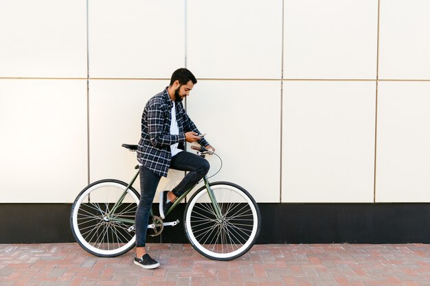 자전거에 앉아있는 동안 휴대 전화를 사용하여 세련된 수염 남자의 프로필보기
