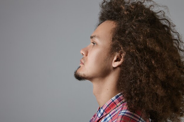 Profile view of stylish serious young mixed race bearded male with curly hairdo dressed in checkered shirt