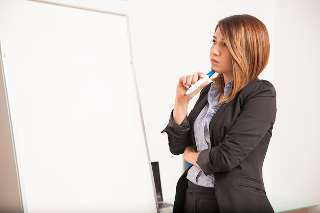 Free photo profile view of a young brunette in a suit standing in front of a flip board thinking what to write