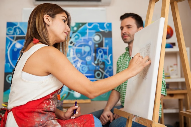 Profile view of a young female artist sketching a male model in her studio