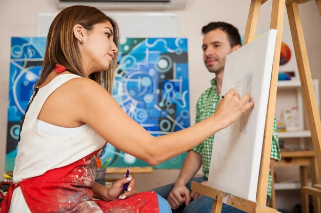 彼女のスタジオで男性モデルをスケッチしている若い女性アーティストの縦断ビュー