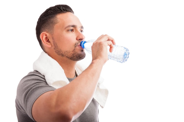 Profile view of a young man with a beard drinking water from a bottle after working out
