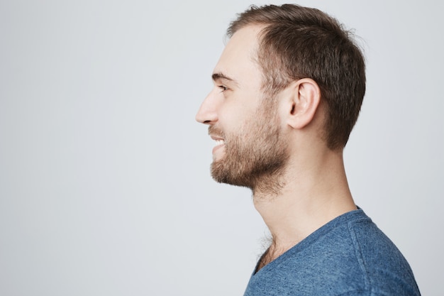 Foto gratuita profilo di giovane uomo barbuto che sorride, guardando a sinistra