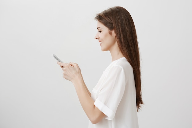 Profile of young pretty woman texting, using mobile phone, order online