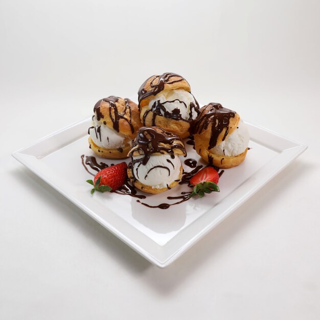 Profiteroles with cream and chocolate glaze on a plate isolated on a white background