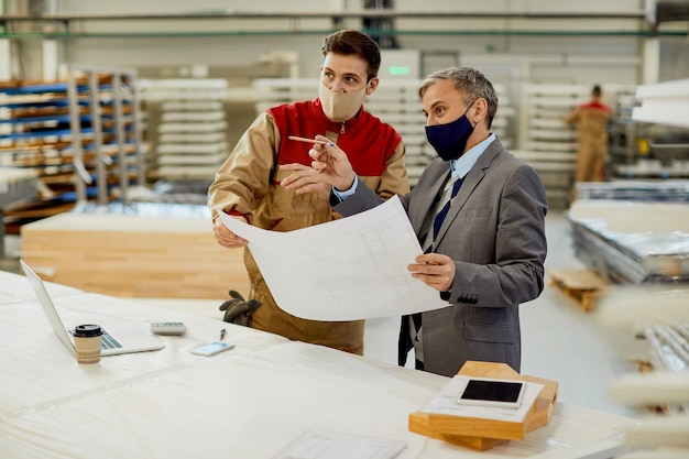 Project manager e falegname che esaminano i piani di progettazione in una struttura per la lavorazione del legno