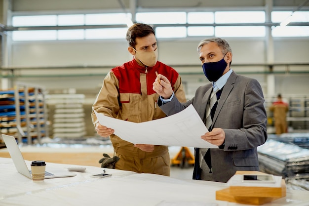 Free photo project manager and carpenter wearing face masks while examining blueprints in a workshop