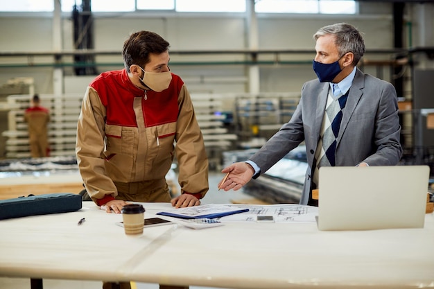 Project manager talking to carpenter while examining blueprints in a workshop