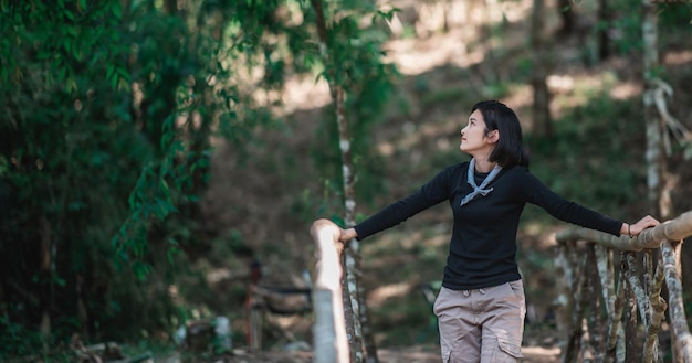 Protrait young woman standing on bamboo bridge smile and looking beautiful nature while camping in forest with happy copy space