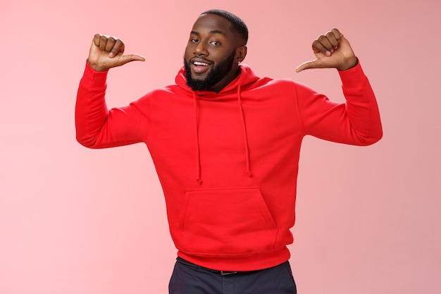 Proud confident arrogant good-looking african american bearded male coworker in red hoodie raise thumbs pointing himself bragging look cheeky talking accomplishments himself, standing pink wall