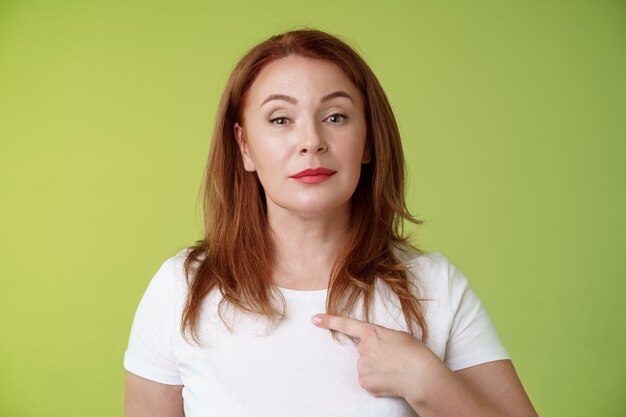 Proud mom pointing herself motivated confident redhead assertive middleaged woman indicating chest volunteering bragging own abilities achievements look camera selfassured green wall