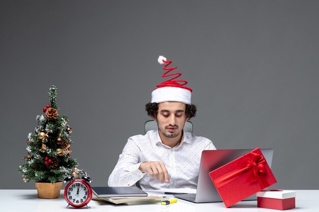 Proud satisfied young businessman with funny santa claus hat in the office on dark background