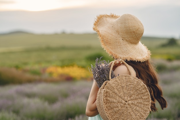 Provence woman relaxing in lavender field. Lady with a straw hat. Girl with bag.