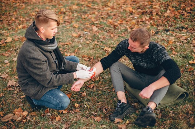 Providing first aid in the park. Man bandaged  injured arm. Guy helps a friend.