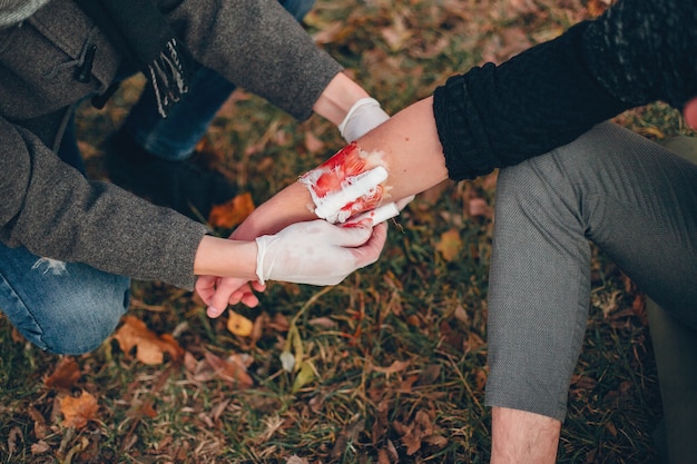 Free photo providing first aid in the park. man bandaged  injured arm. guy helps a friend.