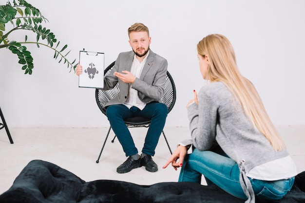 Free photo psychotherapist showing rorschach test card to female patient in clinic