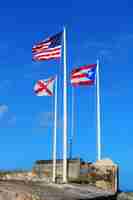 Foto gratuita la bandiera dello stato di porto rico, della nazionale statunitense e della città di san juan sventola con il cielo blu nel castello di san juan el morro.